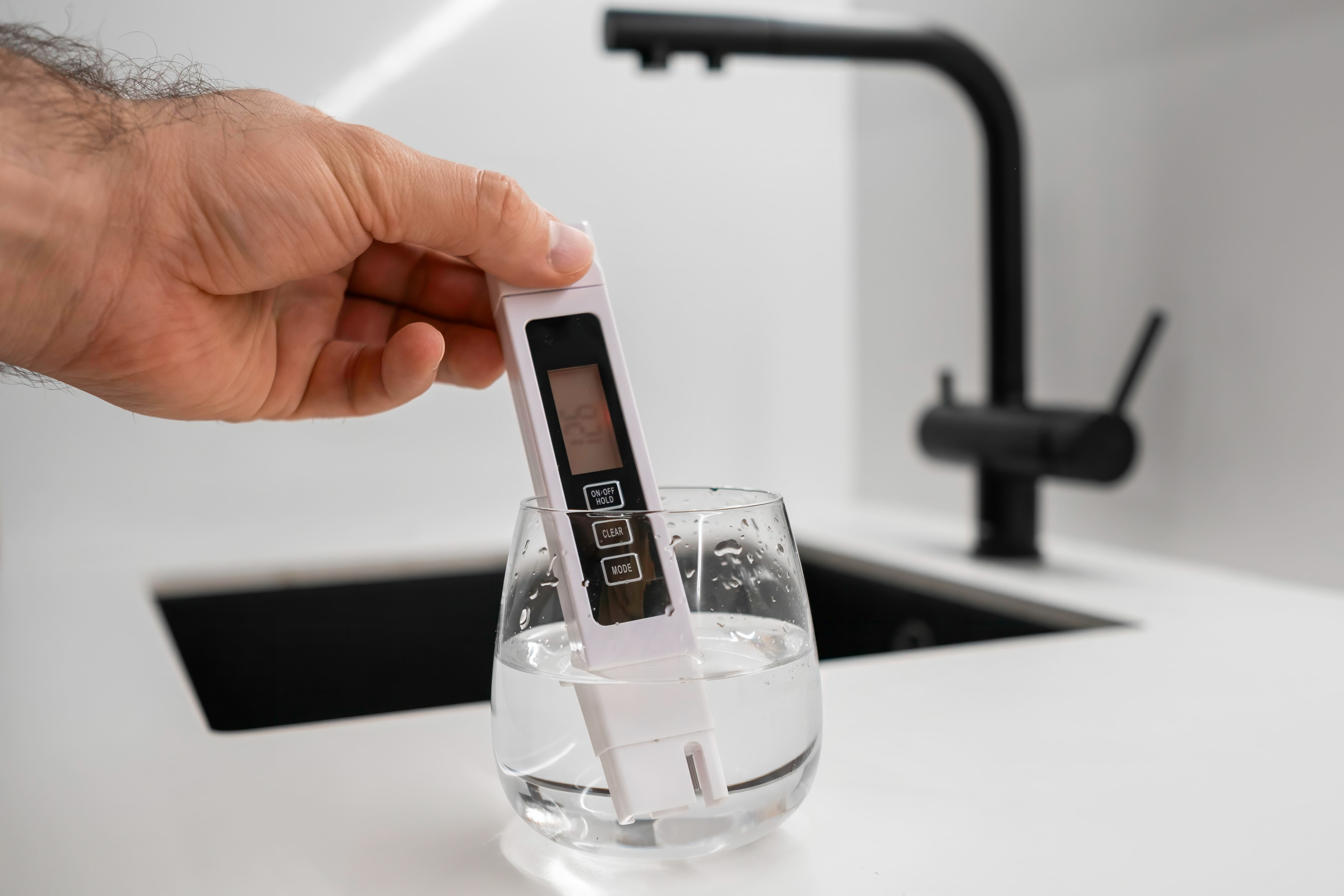 Digital TDS meter measuring dissolved solids in a glass of tap water — St. George, UT water at 24.1 GPG (412 ppm)